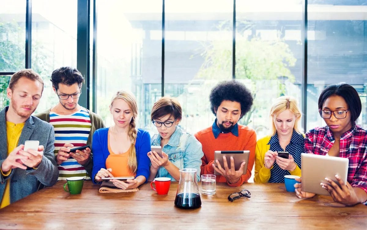 Diverse group using tablets and smartphones at table.