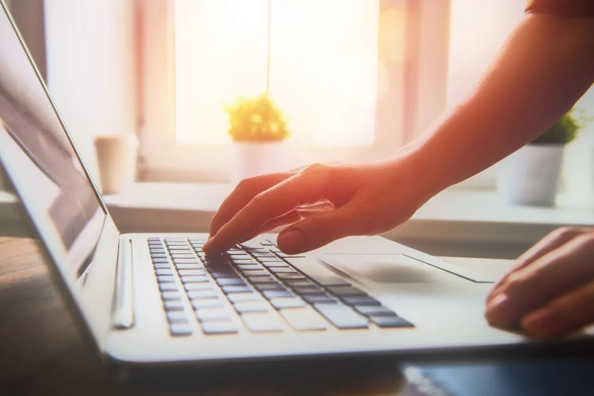 Person typing on laptop near window