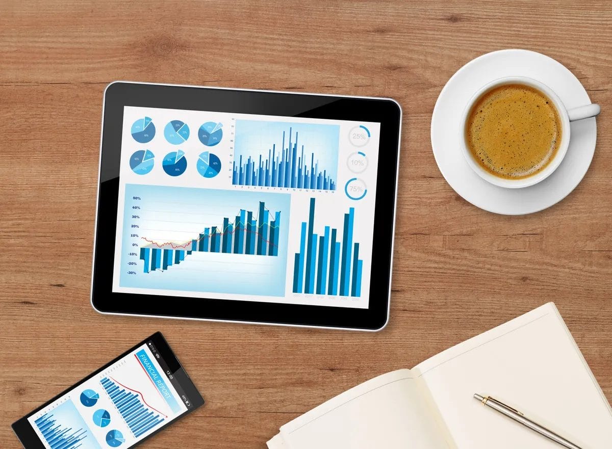 Tablet displaying financial graphs with coffee and notebook.