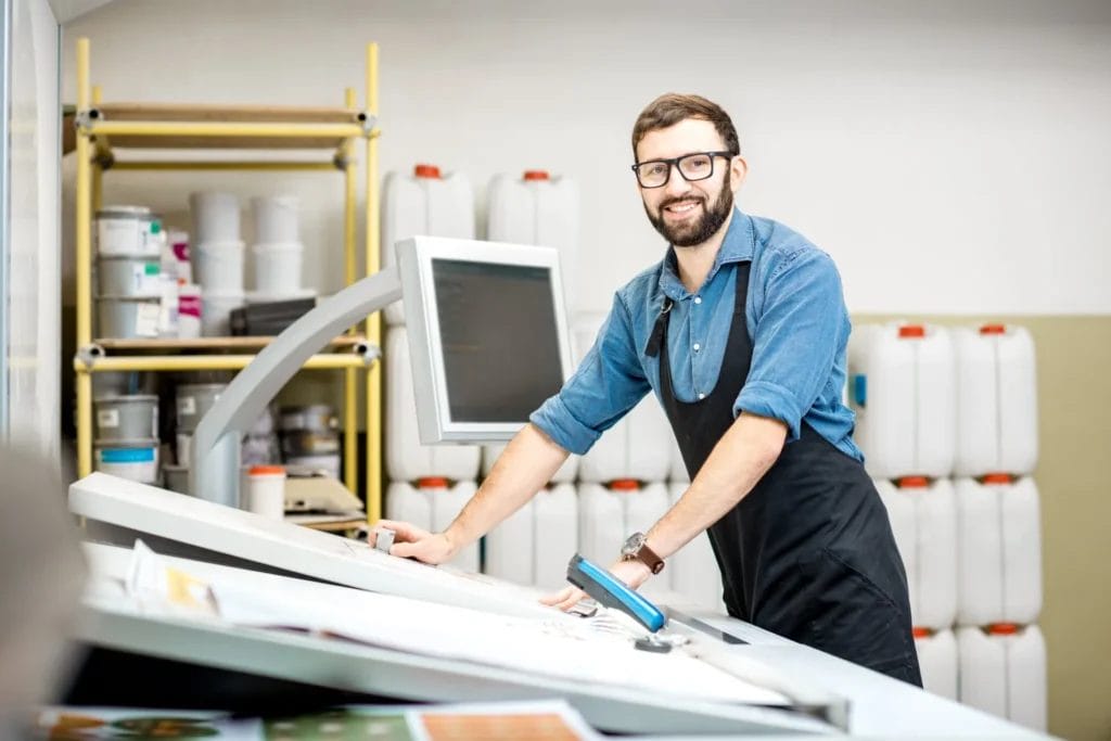 Smiling worker at printing station with screen display.